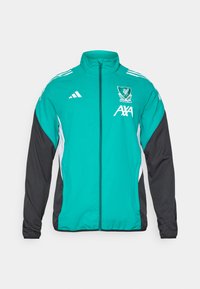 Adidas-jakke med en teal farve på kroppen, sorte ærmer, lynlås lukning og hvide detaljer; viser Liverpool Fodboldklubs våbenskjold og sponsorlogo.