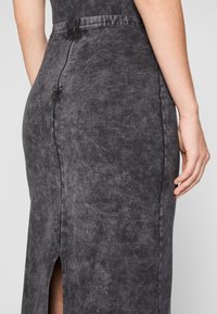 Fustă din denim negru, ajustată, cu un model texturat subtil, slit posterior și un fermoar ascuns pe centrul spatelui.