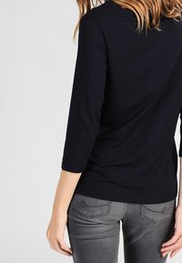 Svart tröja med långa ärmar och rund halsringning, gjord av slät tyg. Matchas med mörkgrå jeans med en diskret design på bakfickan.