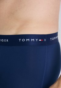 Tengerészkék boxer alsónadrág puha, elasztikus derékpánttal, ami "TOMMY" felirattal és piros-fehér logó részlettel rendelkezik. Sima textura és testhezálló kialakítás.