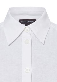 Witte linnen blouse met een klassieke kraag, voorzien van drie knopen aan de voorkant en een label. De stof heeft een lichte textuur. Klein inktvlekje aanwezig.