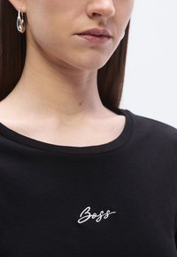 Črna majica s okroglim izrezom in belim vezenim logotipom "Boss" na prsih. Gladek bombažni tekstura, minimalističen dizajn.