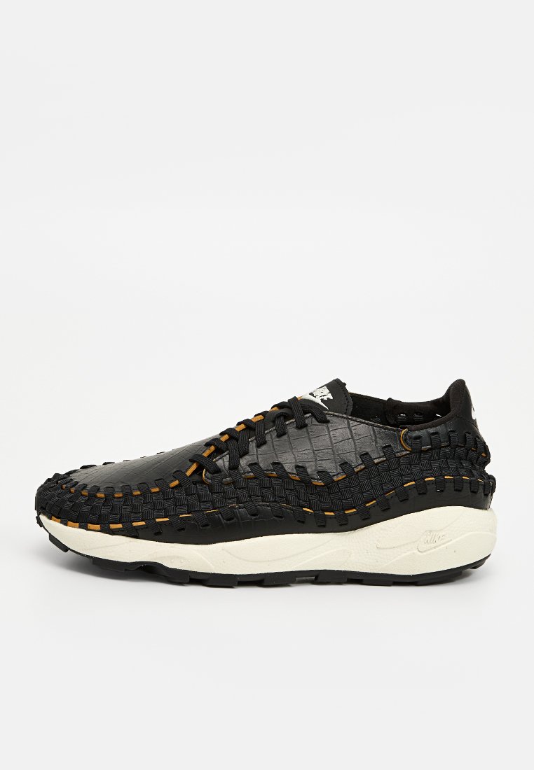 Baskets noires en tissu tissé avec une surface texturée, dotées de coutures orange, d'un semelle intermédiaire blanche et d'une languette au talon.