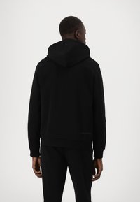 Sweatshirt preto com capuz grande, feito de tecido macio, punhos canelados nas mangas e um logo discreto na bainha.
