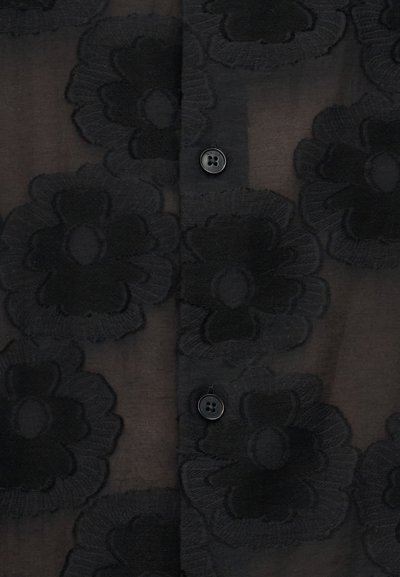 Μαύρο διάφανο ύφασμα με μεγάλα κεντημένα λουλουδένια σχέδια και δύο εμφανή μαύρα κουμπιά σε μια πατιλέτα ρούχου.