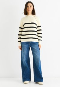 Cream striped sweater with black horizontal stripes and button accents on the shoulder, paired with wide-leg blue jeans.
