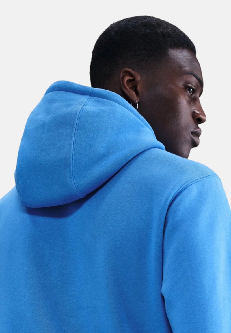 Giovane uomo con felpa con cappuccio blu acceso, di profilo di lato, mostrando il retro e il profilo laterale con un orecchino a cerchio all'orecchio sinistro.