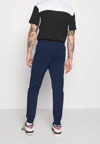 Joggers navy con un diseño ajustado, cinturilla elástica y puños en los tobillos. Llevados con una camiseta de manga corta en blanco y negro y zapatillas deportivas.