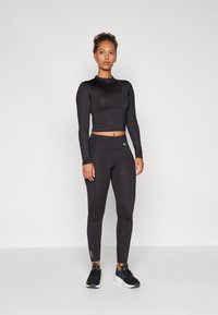 Fekete, hosszú ujjú, cropped felső és magas derekú leggings sima, rugalmas anyagból. A leggingsen logó található, a design pedig letisztult és minimalista.