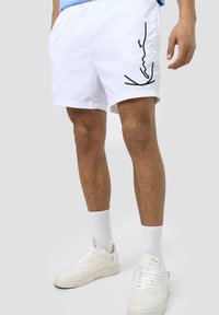 Vita shorts med avslappnad passform, prydda med en svart linjeteckning på sidan. Tillverkade av ett lätt material, kombinerade med vita sneakers.