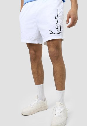 Pantaloni corti bianchi con vestibilità comoda, caratterizzati da un dettaglio disegnato in nero sul lato. Realizzati in materiale leggero, abbinati a sneakers bianche.
