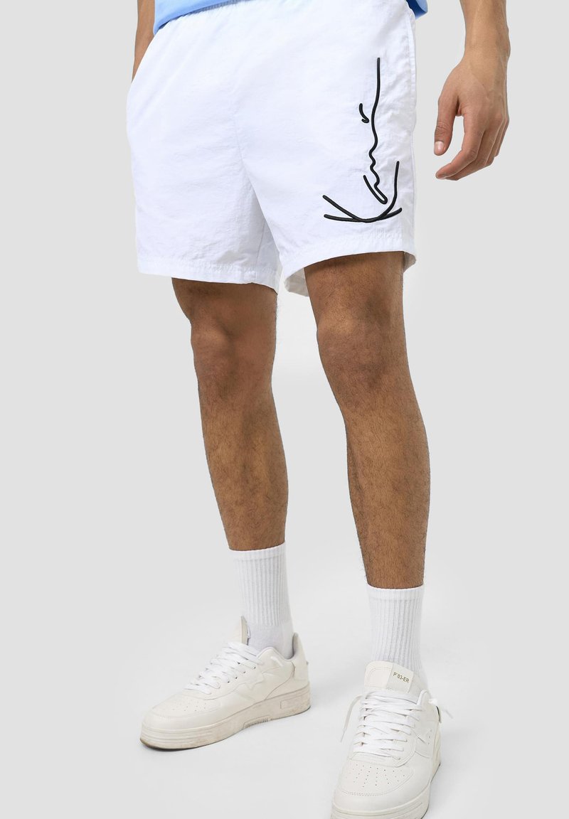 Vita shorts med avslappnad passform, prydda med en svart linjeteckning på sidan. Tillverkade av ett lätt material, kombinerade med vita sneakers.