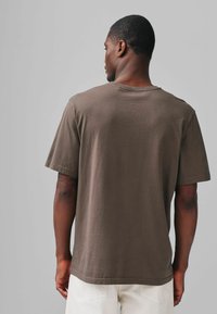 T-shirt din bumbac maro, cu o croială lejeră, mâneci scurte și decolteu rotund, având o textură netedă și un tiv drept.