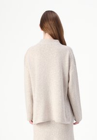 Beige gestrickter Pullover mit runder Ausschnittöffnung, übergroßer Silhouette und Rippdetails an den Bündchen und dem Saum. Weiche Textur.