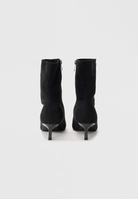 Stivaletti neri in suede con tacco affusolato, dotati di una cerniera sul retro e una texture liscia. La vista posteriore mette in evidenza la forma dello stivale.