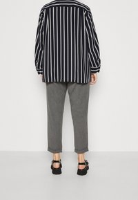 Lässig geschnittene Bluse mit schwarz-weißen Streifen und Kragen, kombiniert mit hochgekrempelten grauen Hosen und schwarzen Sandalen.