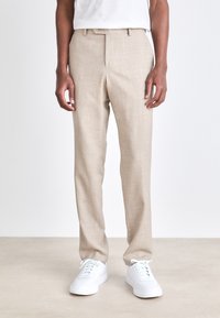 Beige maßgeschneiderte Hose aus strukturiertem Stoff; hat einen geraden Schnitt, flachen Bund und Gürtelschlaufen. Kombiniert mit weißen Sneakern.