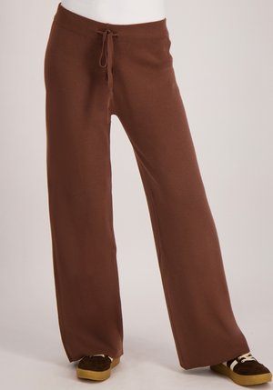 Bruine wijde broek met een trekkoord in de taille, gemaakt van zachte stof. Ze hebben een gladde textuur en een vloeiende silhouet, gecombineerd met donkere schoenen.