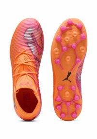 Scarpe da calcio in arancione acceso e rosa. Presentano una tomaia testurizzata, lacci abbinati e una suola a motivo con tacchetti rosa per la trazione.