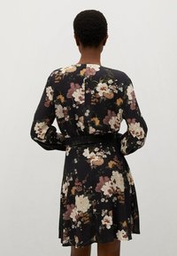 Vestido floral con fondo negro, que cuenta con mangas largas, una cintura ceñida con cinturón y una falda acampanada. Tejido texturizado con patrones de flores multicolores.