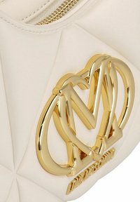 Borsa in similpelle bianca trapuntata con un logo dorato prominente con lettere intrecciate e una chiusura a zip lungo il bordo superiore.