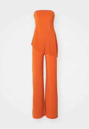 Narancssárga overall, pánt nélküli dizájn, puha anyag, aszimmetrikus felső réteg, széles szárú nadrág, sima textúra, letisztult élek díszítések nélkül.