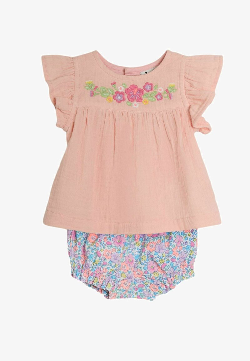 Világos rózsaszín pamut felső fodros ujjakkal, melyet színes virágmintás hímzés díszít, kék virágmintás rövidnadrággal párosítva.