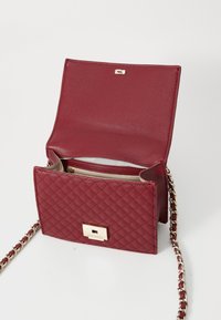 Quilted burgundy handbag with a gold-tone hardware closure, chain strap, and interior compartments. Smooth texture and structured design.