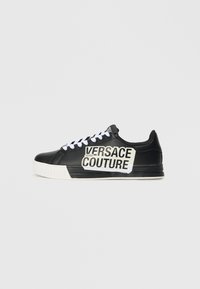 Črne usnjene teniske z belimi vezalkami, z izpostavljenim blagovno znamko Versace Jeans Couture v črni in beli barvi na strani ter belo podplatom.