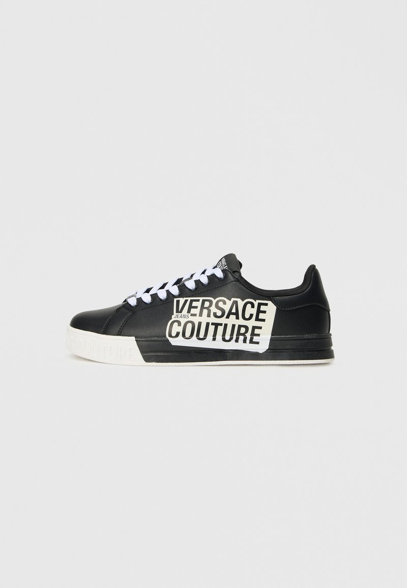 Črne usnjene teniske z belimi vezalkami, z izpostavljenim blagovno znamko Versace Jeans Couture v črni in beli barvi na strani ter belo podplatom.