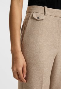 Lichtbruine op maat gemaakte broek met een gestructureerde weving, met een vlakke voorkant en een klein metallic logo-accent op de tailleband.