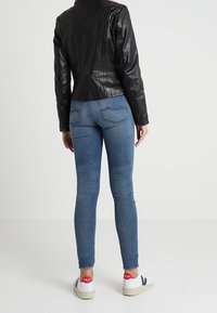 Černá kožená bunda s přiléhavým střihem, modré úzké džíny a bílé tenisky s červenými akcenty. Hladká textura a minimální detaily prošití.