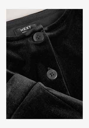 Čierne zamatové oblečenie s hladkou textúrou, vybavené dvoma okrúhlymi čiernymi gombíkmi a výstrihom. Starostlivostná etiketa viditeľná hore.