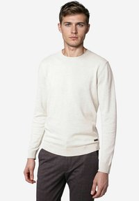 Helle sahnefarbene Sweater mit Rundhalsausschnitt und langen Ärmeln. Gerippte Bündchen und Saum, mit einem kleinen Etikett am unteren Ende.