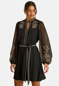 Fekete ruha áttetsző, puffadt ujjal �és hímzett virágmintákkal. Kulcslyuk kivágással és díszített szegéllyel ellátott, egyező övvel.