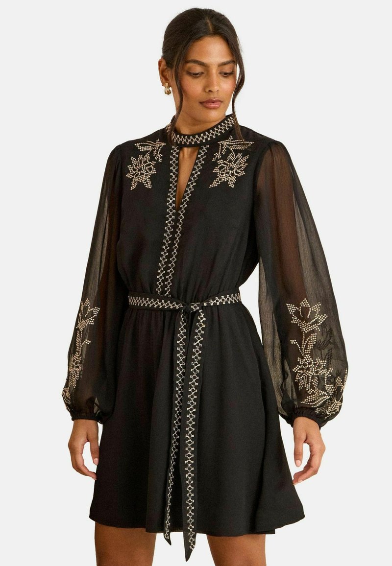 Fekete ruha áttetsző, puffadt ujjal és hímzett virágmintákkal. Kulcslyuk kivágással és díszített szegéllyel ellátott, egyező övvel.