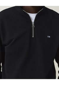 Schwarzer Sweatshirt mit Reißverschluss, geripptem Stoff, silbernem Reißverschluss, hohem Kragen und kleinem Markenlogo auf der Brust.