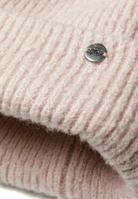 Ribbed pink knit beanie made of soft yarn, featuring a silver button accent with engraved text for branding. Texture appears fluffy.