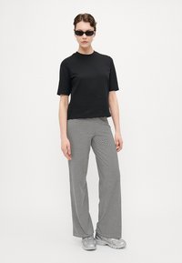 Black cotton t-shirt, short sleeves, paired with wide-leg black and white striped pants. Model wears round sunglasses and metallic sneakers.