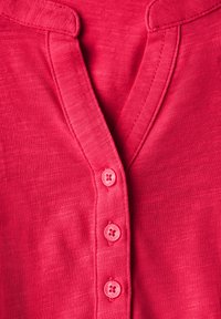 Chemise fuchsia à boutonnage, présentant un col en V, cinq boutons assortis et un tissu texturé. Fini lisse et coupe décontractée.