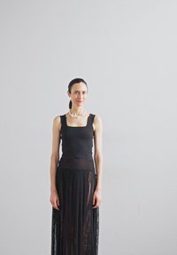 Svart ärmlös topp i kombination med en lång, veckad svart genomskinlig kjol. Tillbehör inkluderar ett halsband i ljusare färg. Enkelt, elegant mönster.