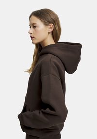 Brun huvtröja med stor huva, ribbade mudd och sidofickor. Mjuk textur, avslappnad passform och minimalistisk design utan synliga logotyper.