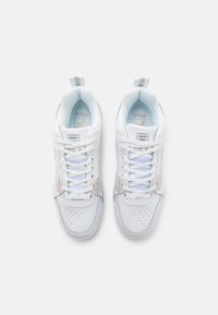 Baskets synthétiques blanches avec des panneaux en mesh, bout rond, perforations pour la respirabilité et accents pastel contrastants. Détail de logo proéminent visible.