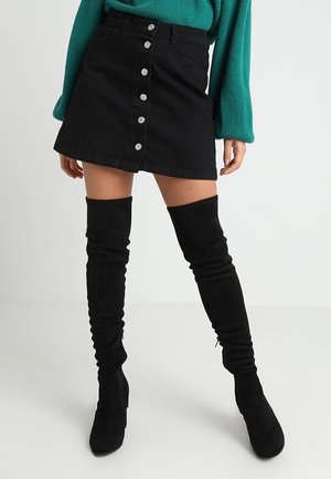 Zwarte denim A-lijn minirok met knoopsluiting aan de voorkant en zakken. Gecombineerd met zwarte suède over-the-knee laarzen. Textuur: glad en zacht.