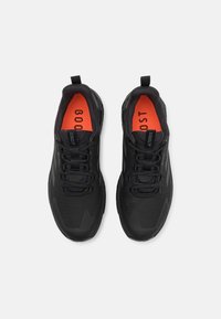 Schwarze Sportschuhe aus strukturiertem Material, mit kontrastierenden orangefarbenen Einlegesohlen und schwarzen Schnürsenkeln. Sie verfügen über ein schlankes Design und eine verstärkte Zehenkappe.