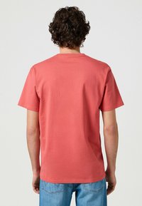 Korallfärgad bomullströja med rund hals och korta ärmar, med en mjuk textur och avslappnad passform, sedd bakifrån.