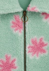 Giacca in pile con sfondo verde menta, caratterizzata da motivi floreali rosa. Include una cerniera color oro e una finitura morbida e testurizzata.