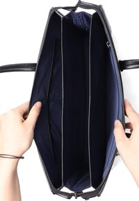 Sort læderhåndtaske med lynlås, der har et marineblåt interiør, to rum og en indvendig lomme til organisering.