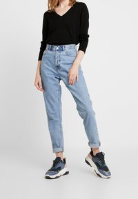 Czarny długi sweter z dekoltem w serek w połączeniu z jasnoniebieskimi dżinsami z wysokim stanem, podwiniętymi na mankietach. Wielokolorowe chunky sneakers.