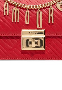 Borsa a tracolla in pelle rossa texture con una catena dorata che riporta la parola "AMOUR" e un ciondolo a forma di cuore, chiusa da un gancio dorato.